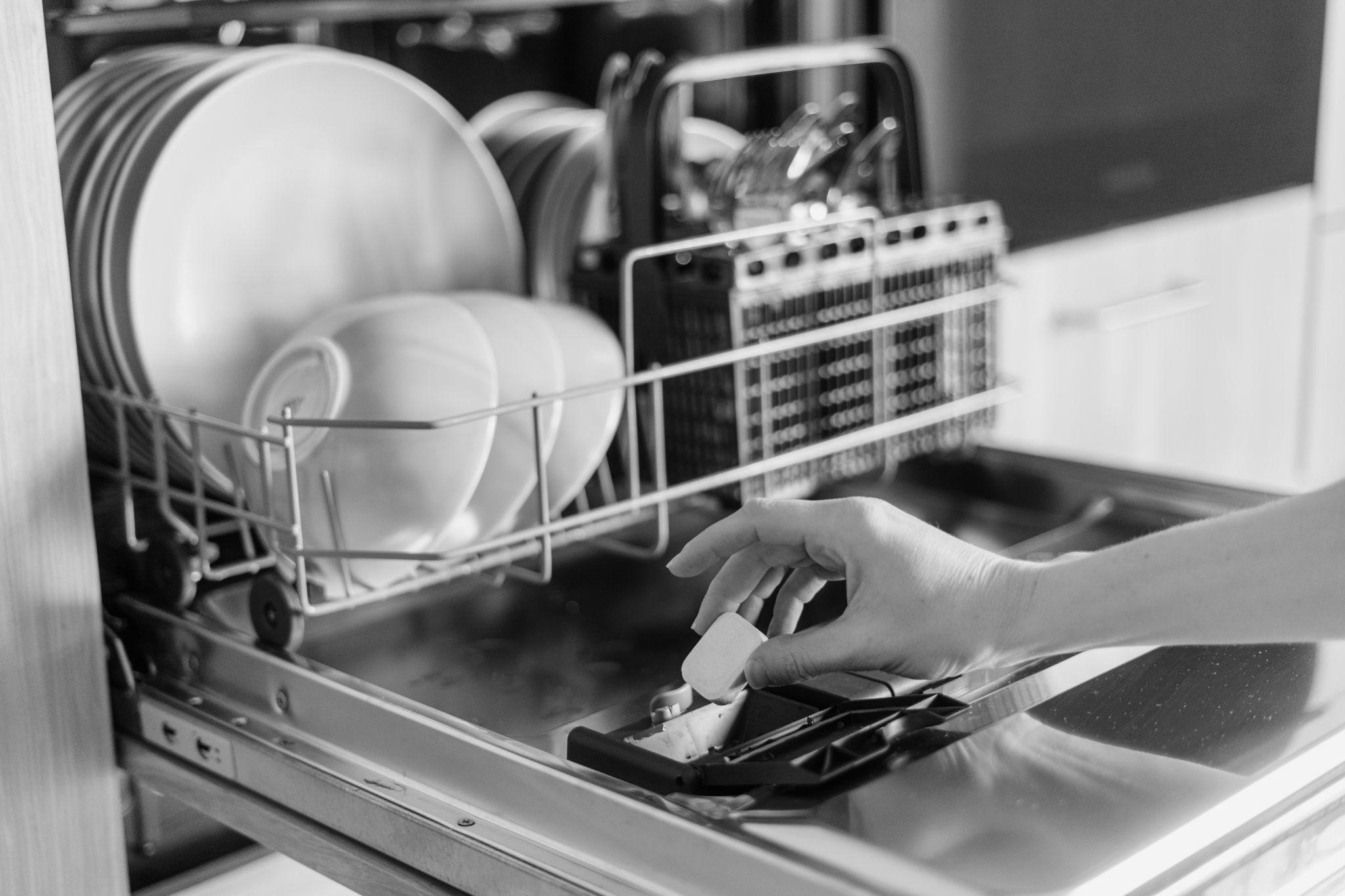 Female hand inserting dishwasher tablet into open built-in dishwasher machine