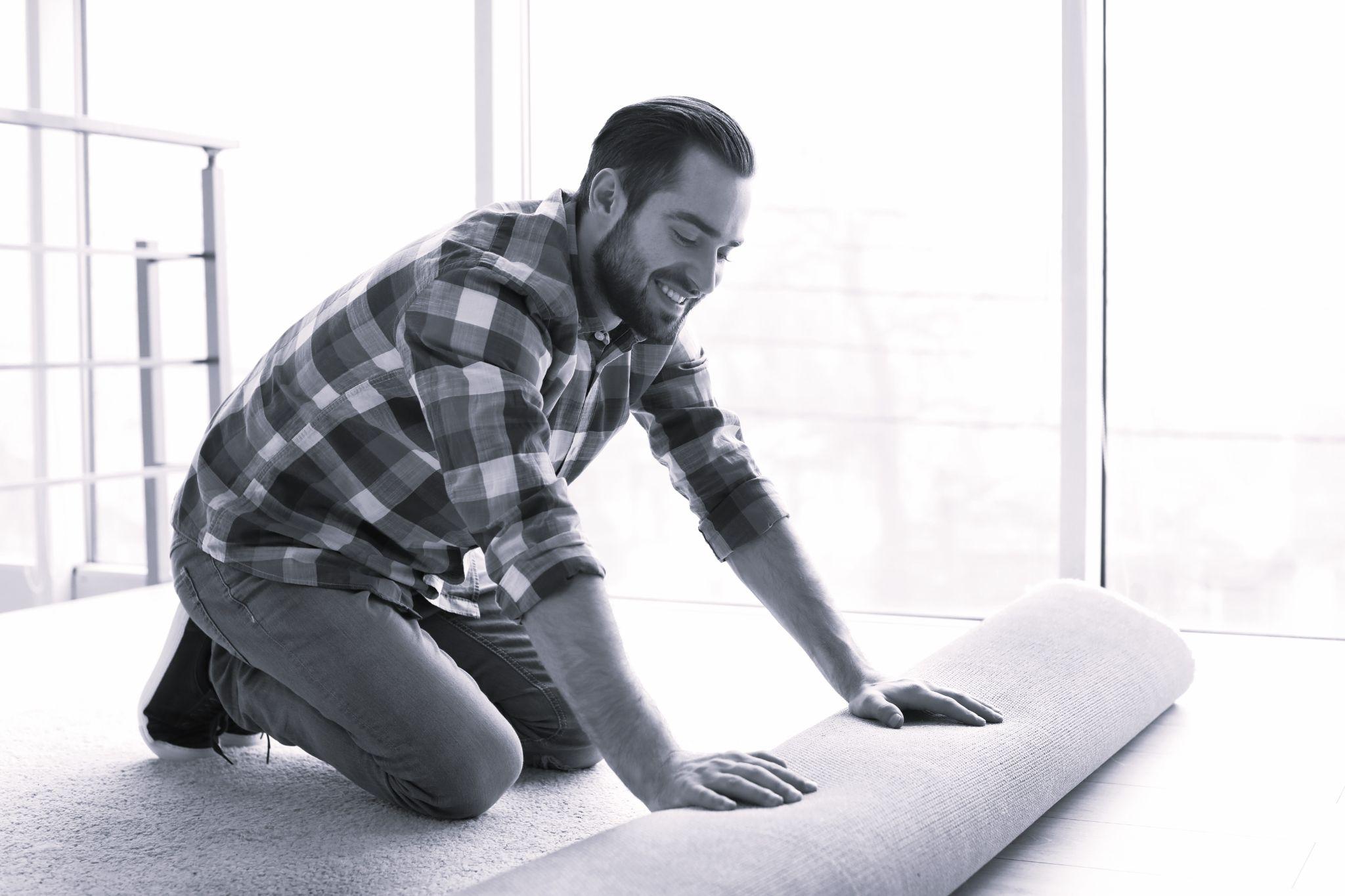 Man rolling out new carpet flooring in room