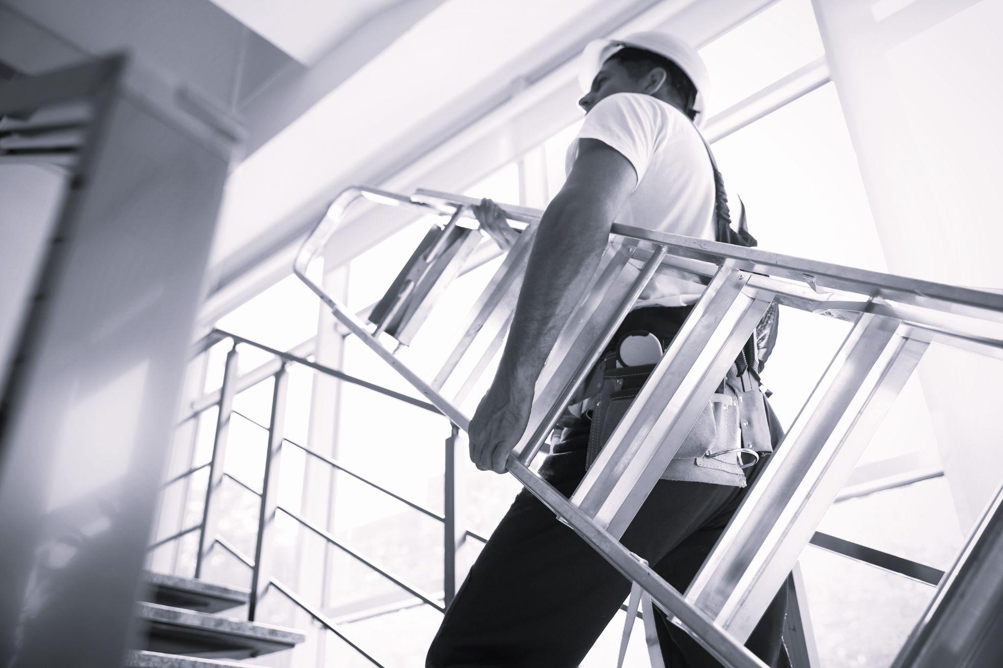 Professional builder carrying metal ladder up stairs, low angle view