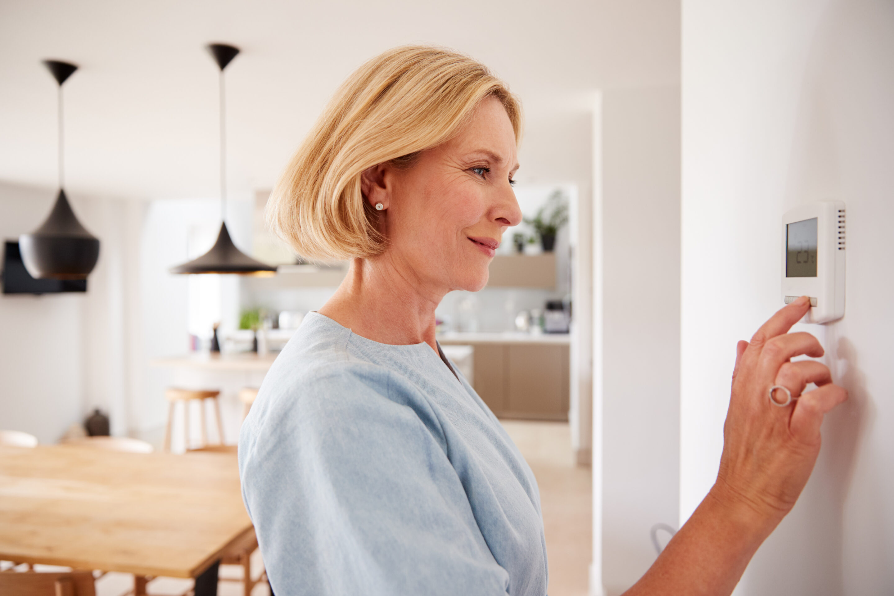 a woman changing the temperature on a thermostat in a new home
