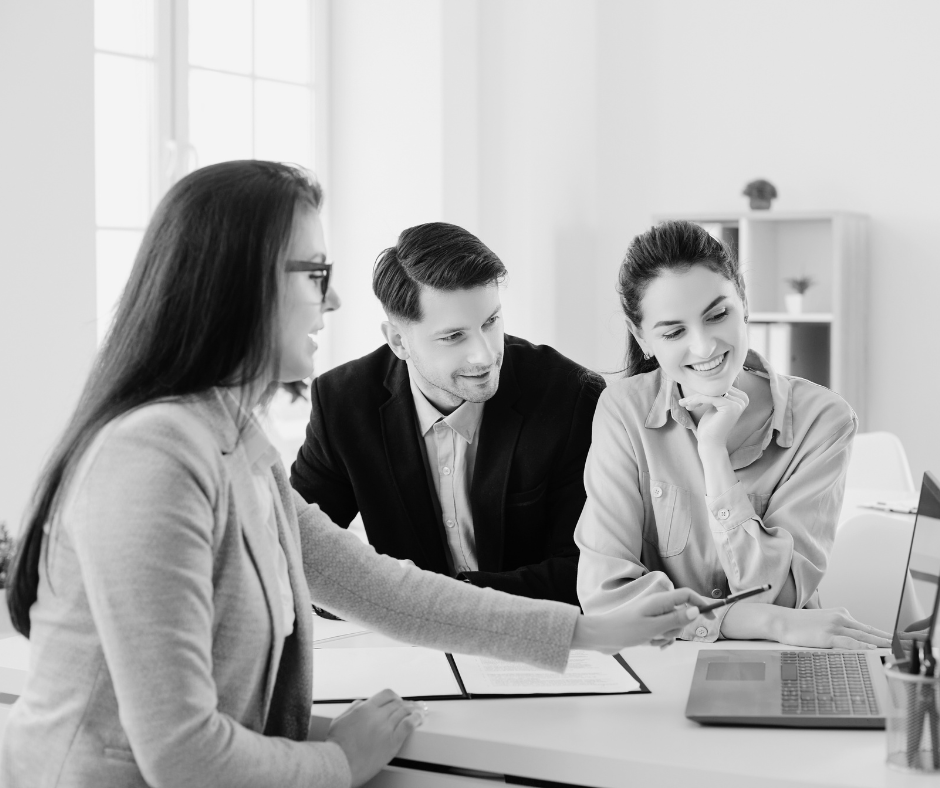 Property manager explaining something on a computer to tenants Three people in a modern office, smiling and focused on a laptop screen. They appear engaged and collaborative, suggesting a positive work environment.