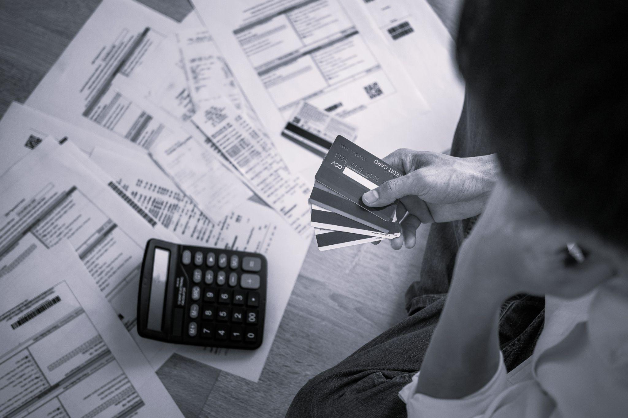 A woman holding her credit cards looking at a pile of bills.