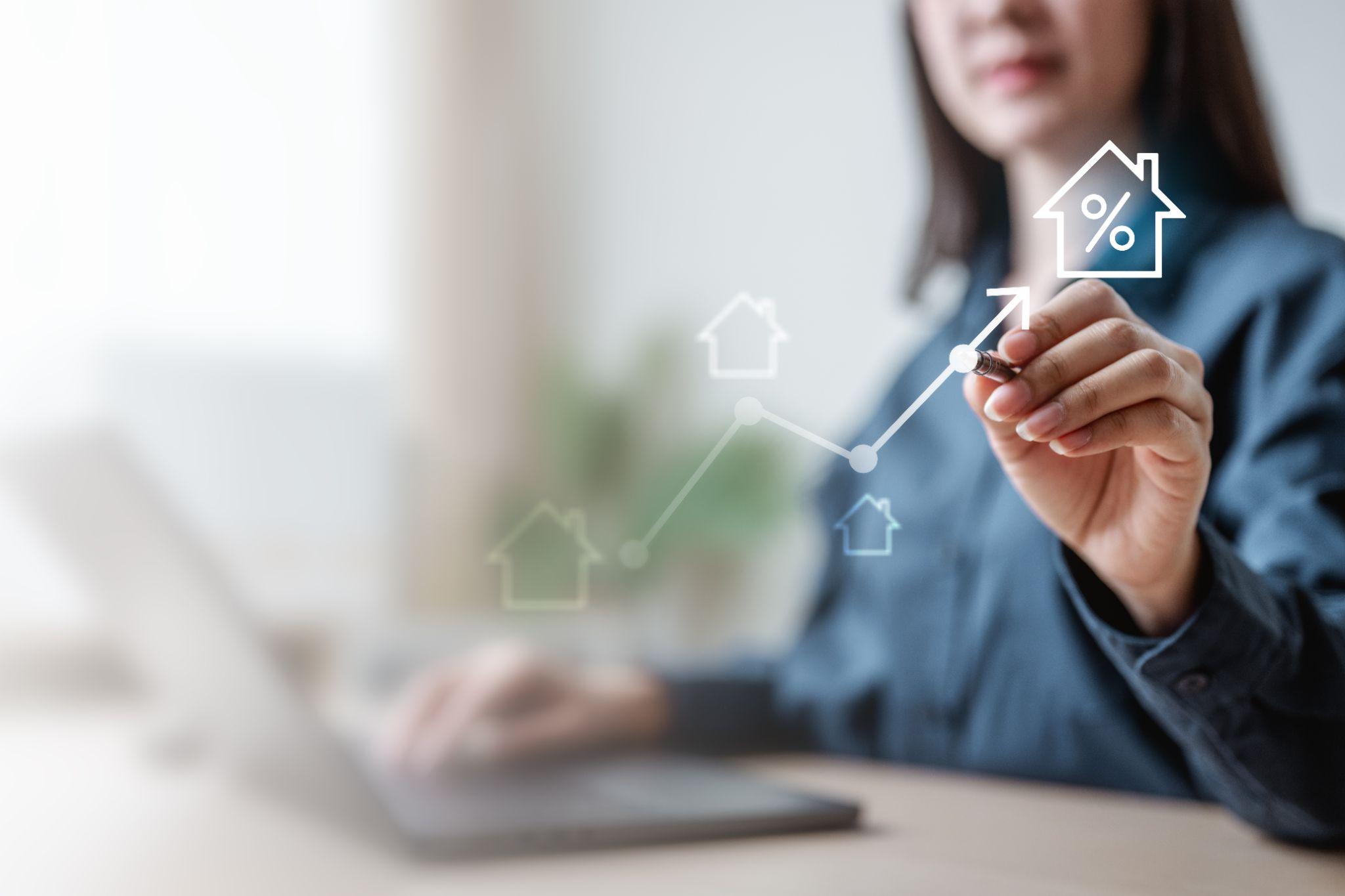 A woman drawing an upward arrow pointing to a house symbol with a percentage sign in it A woman drawing an upward arrow pointing to a house symbol with a percentage sign in it